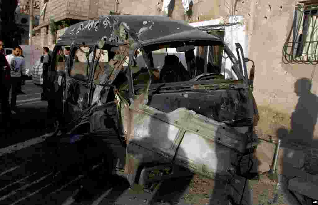 This photo released by the Syrian official news agency SANA shows Syrians standing near a damaged vehicle after an attack in Damascus, Syria, November 7, 2012.
