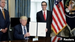 U.S. President Donald Trump displays a financial services executive order as Treasury Secretary Steven Mnuchin looks on during a signing ceremony at the Treasury Department in Washington, April 21, 2017.