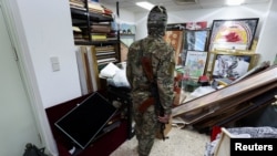 A rebel fighter looks at personal souvenirs of Syria's Bashar al-Assad at one of the rooms of the Presidential Palace known as Qasr al-Shaab "People's Palace," after rebels seized the capital and ousted Assad, in Damascus, Dec. 10, 2024.