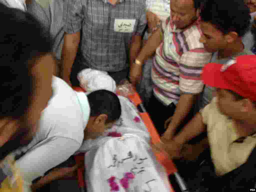 A Morsi supporter kisses the body of a woman killed in early morning clashes with security forces at Rabia el-Adawiya mosque in Cairo, July 27 2013, (Elizabeth Arrott/VOA).