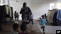 Una mujer hondureña que espera para entrar a Estados Unidos (centro), se peina mientras sus unos niños juegan cerca, en un albergue en Tijuana, México, el 17 de febrero de 2021.