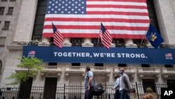 People wearing protective face masks pass the New York Stock Exchange, as employees arrive for the partial reopening of the trading floor, May 26, 2020.