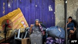 A woman and child wait with belongings before evacuating from Rafah in the southern Gaza Strip on May 11, 2024, amid the ongoing conflict in the Palestinian territory between Israel and Hamas.