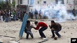 Protesters hide behind a portion of a fence as police fire tear gas and throw stones back at protesters, who have been throwing stones at the police, near Tahrir Square in Cairo Egypt, November 20, 2011.