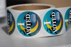 FILE - A roll of stickers sits on the table of an election judge for distribution to voters as they cast their ballots in the atrium of Ball Arena, the home of the NBA’s Denver Nuggets and the NHL’s Colorado Avalanche, October 30, 2020, in Denver.