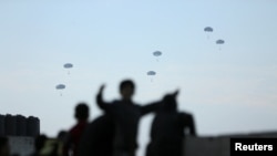 Люди у Газі спостерігають, як американські військові десантують допомогу з літаків на тлі війни між Ізраїлем і палестинським угрупованням ХАМАС, 2 березня 2024 р. REUTERS/Kosay Al Nemer
