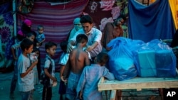 Seorang aktivis Rohingya membagikan baju baru kepada para pengungsi di sebuah kamp pengungsi di tepi Sungai Yamuna, 1 Juli 2021. (Foto: AP/Altaf Qadri)