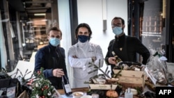 Vendors of a delicatessen wait for customers outside their shop in a commercial street in central Paris on Dec. 24, 2020.