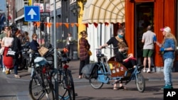 FILE - People, some wearing face masks, observe social distancing to prevent the spread of the coronavirus when standing in line to buy traditional King's Day pastry in Amsterdam Netherlands, April 27, 2020. 