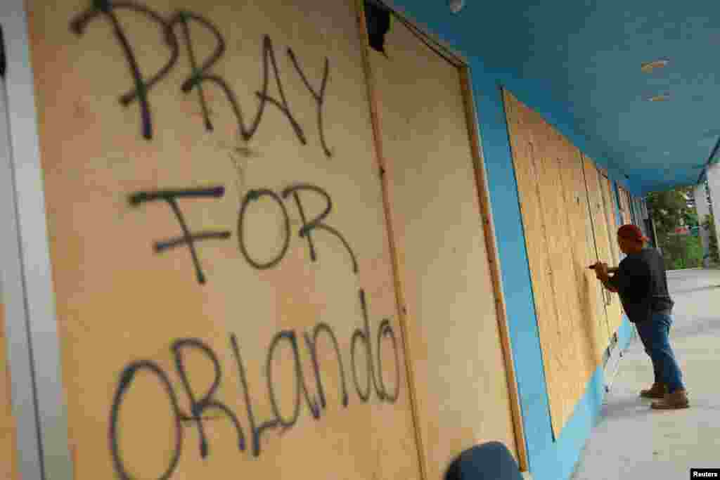 Una persona asegura planchas de madera a las vidrieras de un comercio y se lee que alguien escribió: "Oren por Orlando", en Orlando, Florida, el 8 de octubre de 2024.