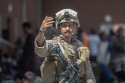 In this image provided by the US Marine Corps, a Marine guides families during an evacuation at Hamid Karzai International Airport in Kabul, Afghanistan, Aug. 23, 2021.