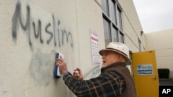 Tom Garing cleans up racist graffiti painted on the side of a mosque in what officials are calling an apparent hate crime, Feb. 1, 2017, in Roseville, Calif. The Tarbiya Institute was spray-painted with a dozen obscene and racist slurs. Garing, a retiree 