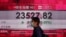 A woman wearing face mask walks past a bank electronic board showing the Hong Kong share index at Hong Kong Stock Exchange Thursday, March 26, 2020.
