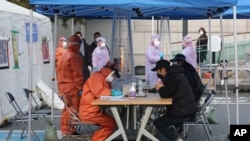 Medical staff wearing protective suits talk with people with suspected symptoms of new the coronavirus, at a testing facility in Seoul, South Korea, March 4, 2020. 