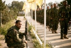 FILE - Syrian Democratic Forces stand in formation at a ceremony to mark their defeat of Islamic State militants in Baghuz, at al-Omar Oil Field base, Syria, March 23, 2019.