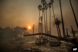FILE - Smoke rises behind a destroyed apartment complex as a wildfire burns in Ventura, Calif., Dec. 5, 2017.