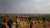 FILE - TV journalists work on a hilltop in Ceylanpinar, Sanliurfa province, southeastern Turkey, as in the background smoke billows from a fire in Ras al-Ayn, Syria, Oct. 20, 2019. 