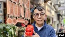 朱榮記老闆朱耀昌手持該店傳奇產品：紅色膠豬錢罌。(美國之音照片)