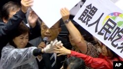 In this image made from video, Taiwanese Premier Su Tseng-chang holds a microphone as opposition party lawmakers from the Nationalist party (KMT) block his attempt to speak during a parliament session in Taipei, Taiwan, Nov. 27, 2020.