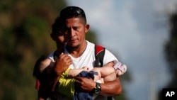 El migrante hondureño Selvin Hernández carga a Mayra Irene, hija de otro migrante, en medio de un grupo de migrantes que intentan llegar a Estados Unidos, cerca de El Cinchado, Guatemala, el 15 de enero de 2020, en la frontera con Honduras.