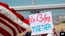 A protester holds a sign outside a closed gate at the Port of Entry facility, June 21, 2018, in Fabens, Texas, where tent shelters are being used to house separated family members.