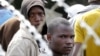 FILE - Displaced foreigners sit behind razor wire surrounding a tented refugee center in Primrose near Johannesburg, April 22, 2015