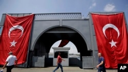 FILE - Men walk at the Galata bridge past two Turkish flags, in Istanbul, Aug. 2, 2016. U.S. and Turkish diplomats are undertaking a complicated effort to improve relations between the two countries.