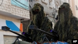 Masked militants from the Izzedine al-Qassam Brigades, a military wing of Hamas, wear camouflage while sitting behind a sniper gun on the back of a truck while marching along the streets of Nusseirat refugee camp, central Gaza Strip, May 28, 2021.