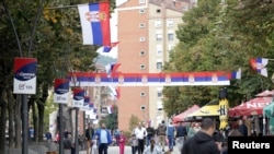 FILE - People walk through a street decorated with Serbian flags in Mitrovica, Kosovo, Oct. 5, 2019.
