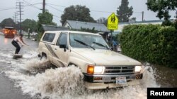 Max Barnett, 23, is pulled on a surfboard by driver Riley Johnson, 23, down a flooded street after the threat of mudslides prompted evacuation orders in east Santa Barbara, California, Jan. 9, 2023.