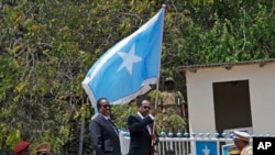 Somalia's President Mohamed Abdullahi Farmajo, center-right, holds a Somali flag during a handover ceremony at the presidential palace with former president Hassan Sheikh Mohamud, center-left, in Mogadishu, Somalia Thursday, Feb. 16, 2017. 