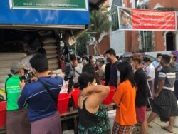 People stock up on rice after a military coup, at a street corner in Yangon, Myanmar, Feb. 1, 2021, with a banner depicting Aung San Suu Kyi, now detained, still on display.