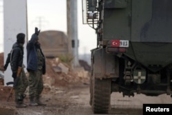 Turkish military vehicles drive by Free Syrian Army fighters, backed by Turkey, in the Syrian rebel-held town of al-Rai as they head towards the northern Syrian town of al-Bab, Jan. 9, 2017.