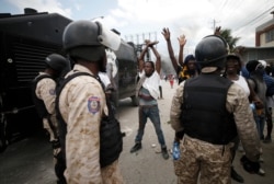 Protestors calling for the resignation of President Jovenel Moise raise their arms in front of a group of police in riot gear, in Port-au-Prince, Haiti, Oct. 4, 2019.