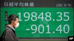 បុរស​ម្នាក់​ដើរ​កាត់​កា្តរ​ផ្សារ​ភាគហ៊ុន​អេឡិចត្រូនិក​នៅ​ក្រុមហ៊ុន​ទីផ្សារ​ភាគហ៊ុន​មួយ​នៅ​ក្នុង​ក្រុង​តូក្យូ កាលពី​ថ្ងៃទី៩ ខែមីនា ឆ្នាំ២០២០។