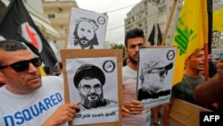 Protesters carry signs showing the faces of Lebanee Shiite movement Hezbollah leader Hassan Nasrallah and slain military commander Mustafa Badreddine as they march in an anti-US demonstration near US Embassy headquarters in Akwar, July 10, 2020. 