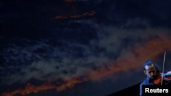 Violinist Simon Garcia plays an adaptation of Antonio Vivaldi's famous “The Four Seasons” concertos as a screen shows an image of a wildfire on International Day against Climate Change in Madrid, Spain, October 24, 2023. REUTERS/Susana Vera