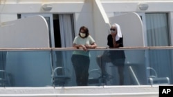 Passengers wearing protective masks look out from their balcony on the Coral Princess cruise ship while docked at PortMiami during the new coronavirus outbreak on April 4, 2020, in Miami.