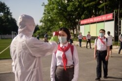 FILE - A student has her temperature taken as part of anti-COVID-19 procedures before entering the Pyongyang Secondary School No. 1 in Pyongyang, North Korea, June 22, 2021.