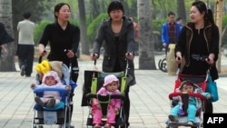 FILE - Women push babies in strollers through a Beijing park during a public holiday.