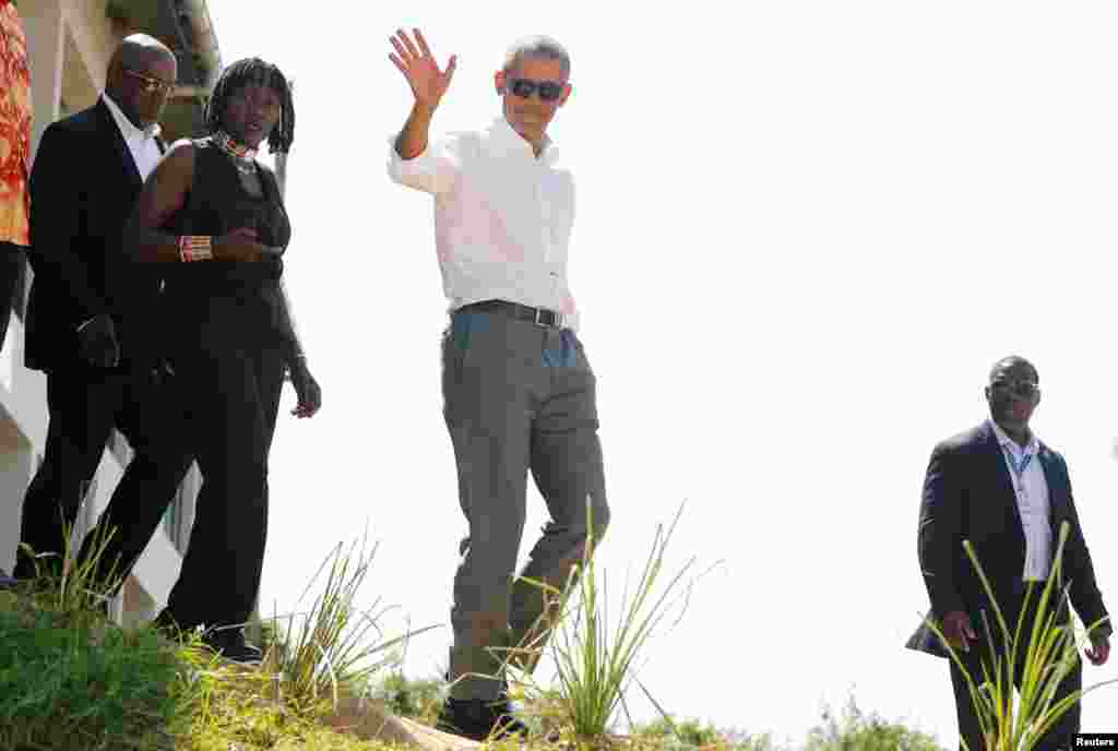 Former U.S. President Barack Obama waves to photographers as he tours the Sauti Kuu resource center near his ancestral home in Nyangoma Kogelo village in Siaya county, western Kenya. With him is Auma Obama.