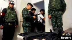 Soldiers stand next to a cache of weapons found in an derelict building where military forces say an explosive device was thrown on to anti-government protesters, in Bangkok, Thailand, Jan. 17, 2014.