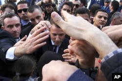 French President Emmanuel Macron is protected by security members as he meets residents in Algiers, Wednesday, Dec.6, 2017. Macron is traveling to Algeria for a one-day working visit aimed at boosting the security and economic cooperation between the two countries.
