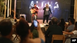 In this Jan. 12, 2019 photo, Venezuelan singer Reymar Perdomo performs with fellow Venezuelan and guitarist Omar Rumbos at a fair on the beach of San Bartolo, Peru. 