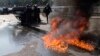 FILE - Riot police stand by an overthrown car during a demonstration by taxi drivers opposed to ride-sharing service Uber in Paris, June 25, 2015.