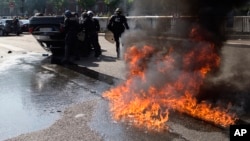 FILE - Riot police stand by an overthrown car during a demonstration by taxi drivers opposed to ride-sharing service Uber in Paris, June 25, 2015.