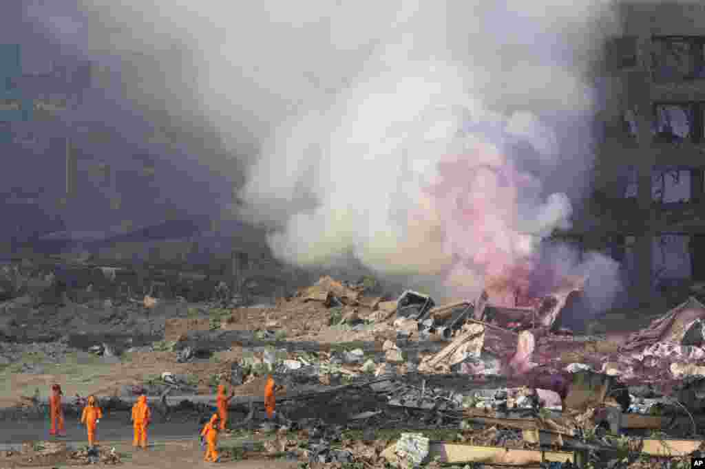 Firefighters in protective gear stand by as pink smoke billows up into the sky after an explosion at a warehouse in northeastern China's Tianjin municipality, Aug. 13, 2015.