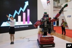 FILE - A woman demonstrates the ability of Baxter, an industrial robot from U.S. company Rethink Robotics, to follow her hand movements during the World Robot Conference in Beijing, Oct. 21, 2016.