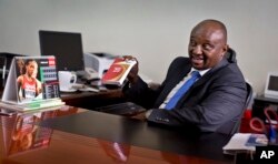 FILE - Athletics Kenya CEO Isaac Mwangi holds up a copy of the IAAF Competition Rules book, to illustrate his denial that Athletics Kenya would have the power to shave time off athletes’ bans, in Nairobi, Kenya, Feb. 8, 2016.