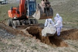 FILE - Municipality workers bury the body of a coronavirus victim on the outskirts of Herat province west of Kabul, Afghanistan, March 27, 2020.